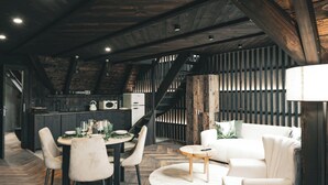 Une cuisine moderne avec des poutres en bois foncé, un coin repas avec des chaises blanches et un canapé blanc.