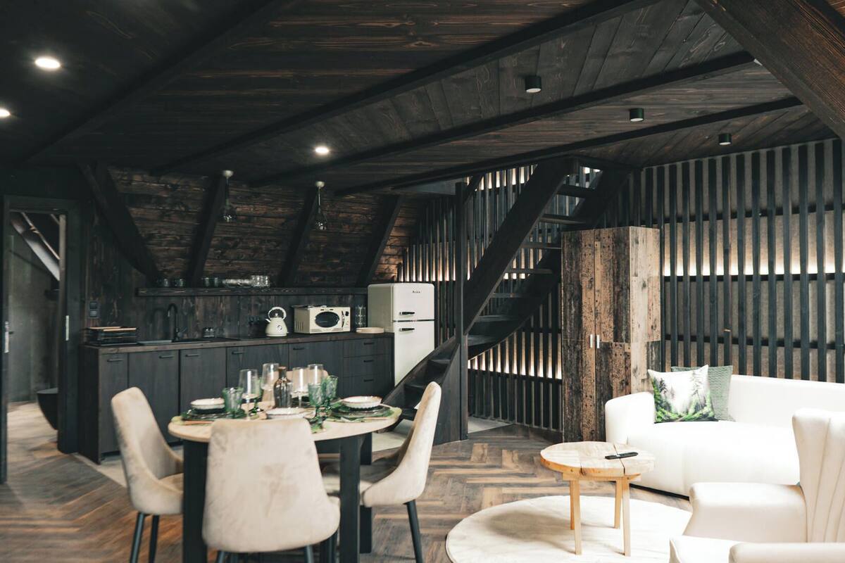 Eine moderne Küche mit dunklen Holzbalken, einem Essbereich mit weißen Stühlen und einem weißen Sofa.