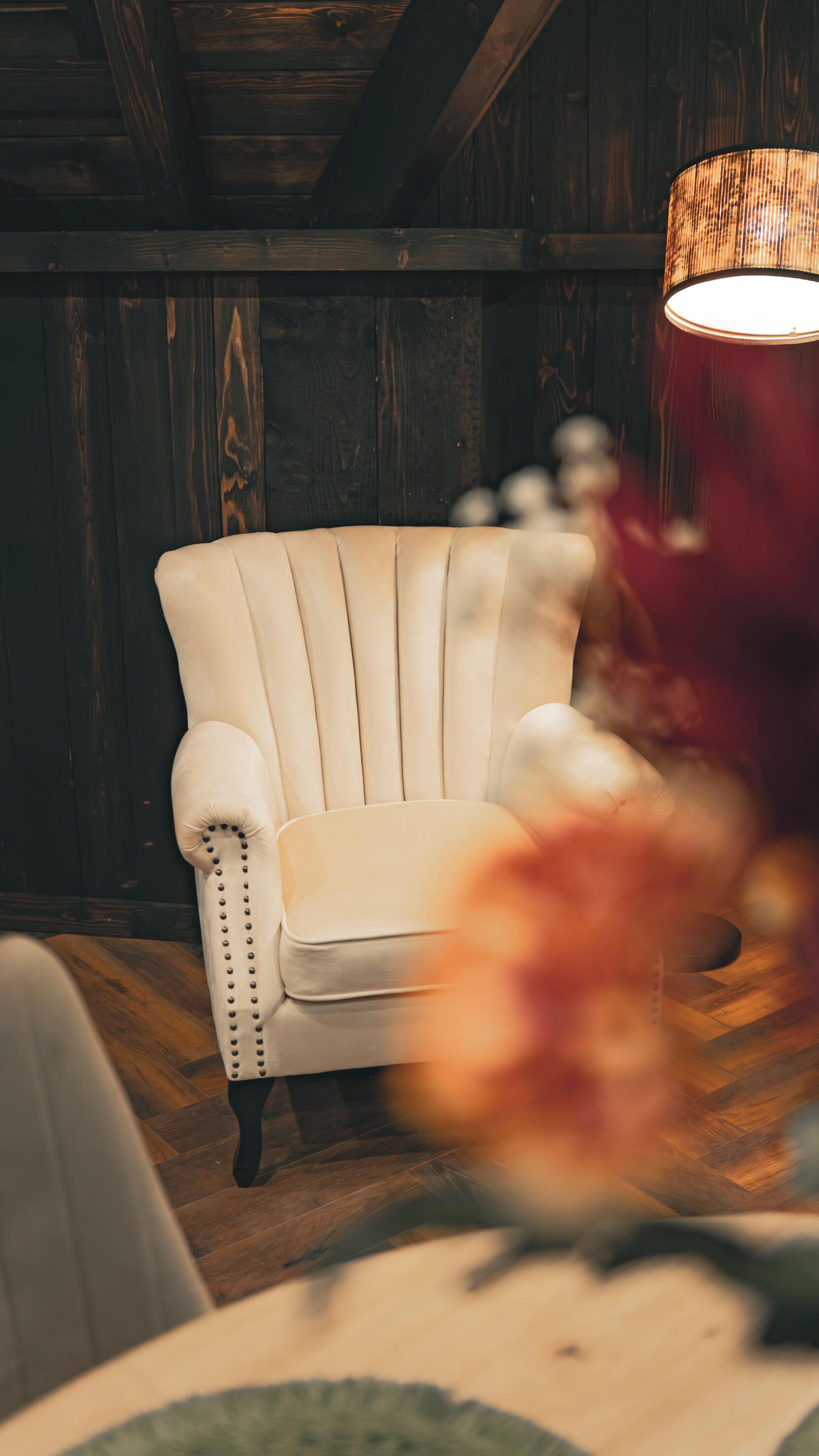 Un sillón blanco con respaldo alto y botones decorativos, situado en una habitación con paredes y suelo de madera.