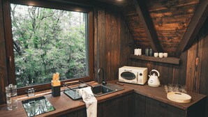Une cuisine rustique avec un intérieur en bois, une fenêtre donnant sur la verdure, un évier, un four à micro-ondes et une bouilloire posés sur le plan de travail.