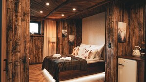 Une chambre rustique avec des murs en bois, un lit recouvert d’une couverture sombre et un petit appareil blanc placé à droite.