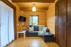 Une pièce chaleureuse aménagée comme une cabane, avec un intérieur en bois, un canapé, une petite table ornée d’un vase de fleurs et un téléviseur fixé au mur.