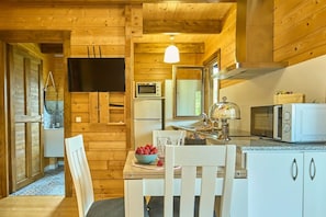 Un intérieur en bois comprenant une table à manger, des chaises, un saladier rempli de fraises, un four à micro-ondes et un téléviseur.