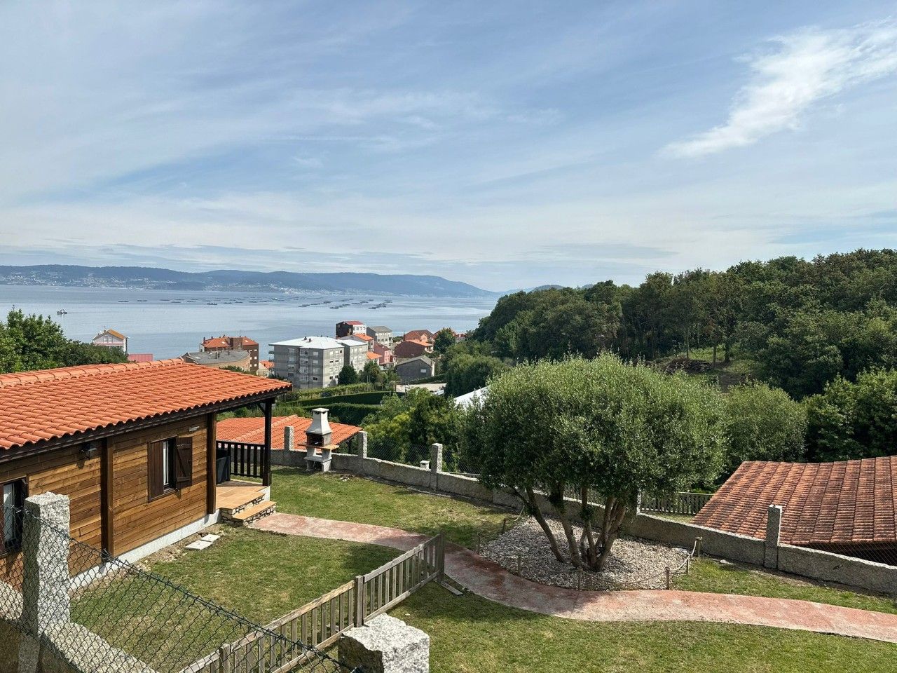 A coastal property with a wooden building, a paved pathway, and a view of the sea and distant hills.