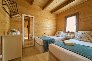 A cabin with two beds, a small table, a window, and a door leading to another room.