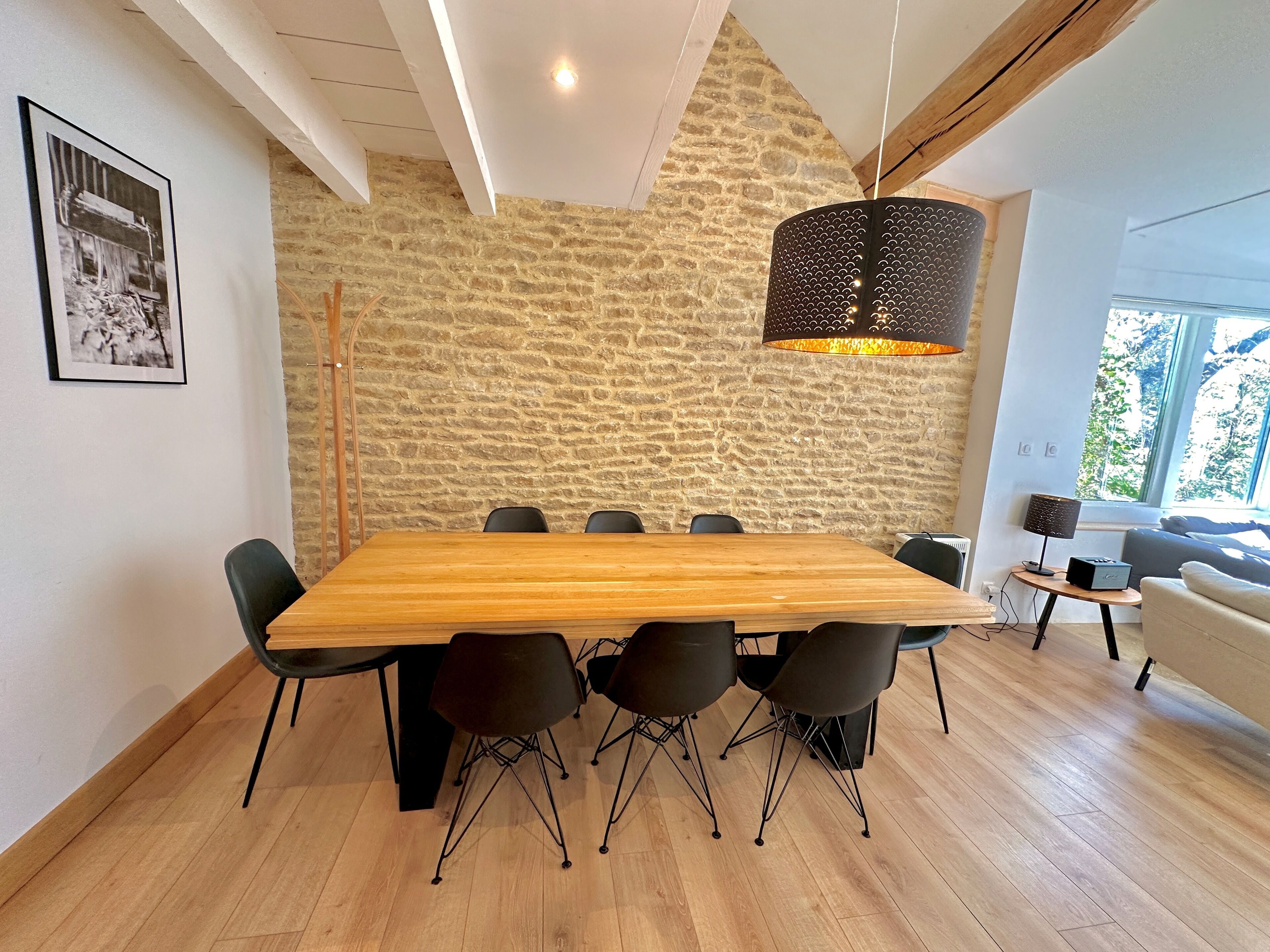 A modern dining area with a large wooden table, black chairs, and a stone wall.