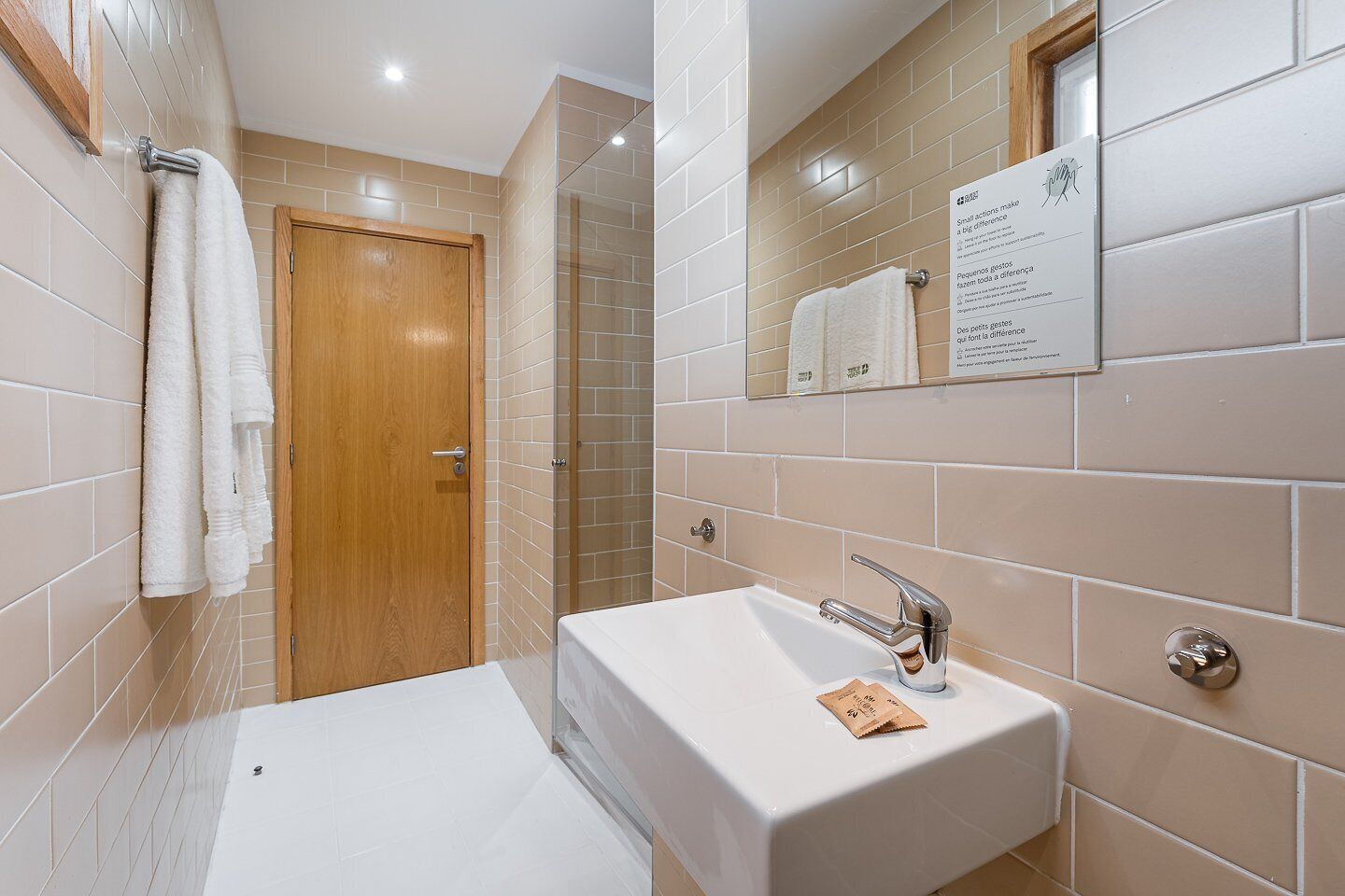 Une salle de bain moderne avec un lavabo blanc, une porte en bois et une cabine de douche en verre.
