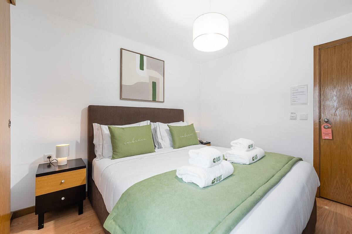 Une chambre d’hôtel avec un lit, une table de chevet, une lampe, une couverture verte et une porte avec une pancarte.