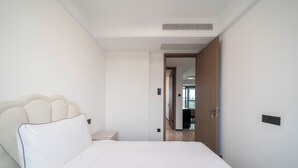 A hotel room with a bed, a nightstand, and a door leading to another room. - Tyms Hongqiao Deluxe 3BR 2BA APT  (Shanghai)