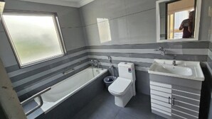 Ein Badezimmer mit Badewanne, Toilette und Waschbecken, mit gestreiftem Wanddesign und einem Fenster.