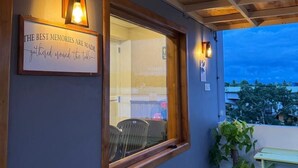 Ein überdachter Außenbereich mit Holzbalken, einem gerahmten Motivationsspruch und einem Fenster mit Blick auf eine Wohngegend.
