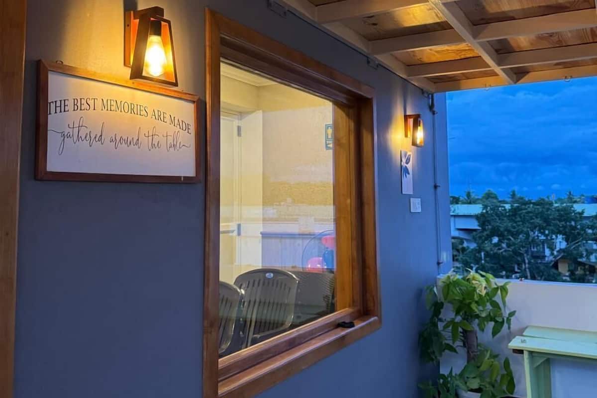 Un espace ext érieur abrité, doté de poutres en bois au plafond, d’une citation inspirante encadrée et d’une fenêtre donnant sur un quartier résidentiel.