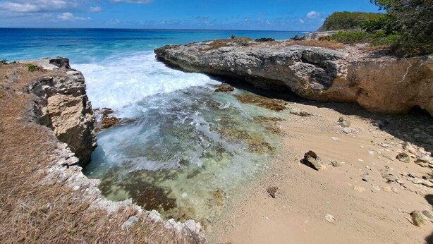 A coastal landscape with clear waters, rocky formations, and a sandy beach.