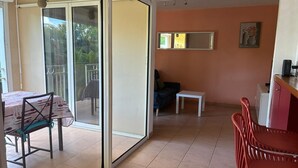 A spacious room with a sliding glass door leading to a balcony, a dining area with a table and chairs, and a kitchenette area.