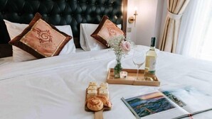 Una cama bien tendida con almohadas, una bandeja con comida y bebida, una vela y un libro.