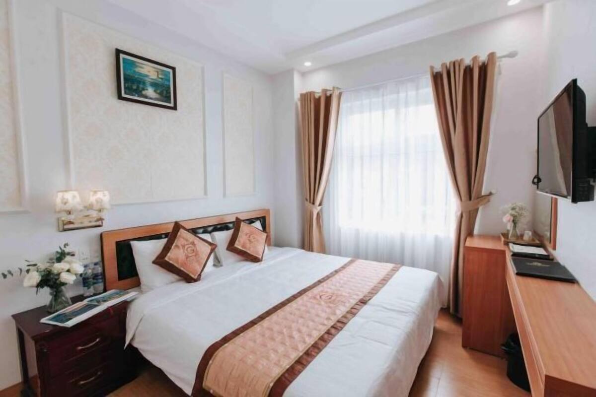 A hotel room with a bed, bedside table, lamp, curtains, and a TV.