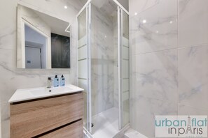 A modern bathroom with a white marble vanity, a glass-enclosed shower, and a large mirror. - Urban Flat 04 - Pretty 2 Bedroom Flat in Montorgueil (París)