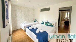 Een moderne hotelkamer met twee bedden, een wand met een geometrisch patroon en uitzicht op een balkon.