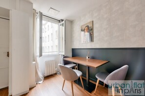 A modern dining area with a wooden table and two grey chairs, a window with curtains, and a wall with a geometric pattern. - Urban Flat 04 - Pretty 2 Bedroom Flat in Montorgueil (París)