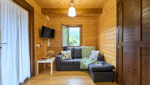 A cozy cabin room with a wooden interior, a sofa, a small table with a vase of flowers, and a TV mounted on the wall. - Cima 1 Cabin in Bueu (Bueu)