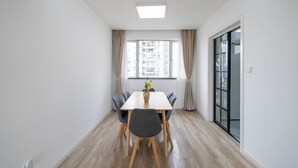 Een moderne, goed verlichte kamer met een houten vloer, een groot raam met gordijnen, een tafel met stoelen en een vaas met bloemen.