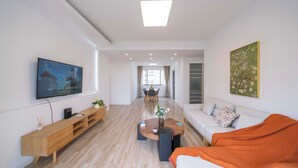 Een moderne woonkamer met een flatscreen televisie, een houten tv-meubel, een ronde salontafel en een bank met een oranje plaid.