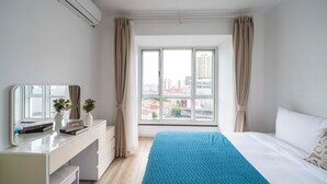 Een hotelkamer met een bed, een bureau met spiegel, een raam met gordijnen en uitzicht op gebouwen.