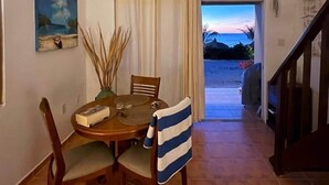 Un espace repas comprenant une table, des chaises et une vue sur la mer, visible à travers une porte.