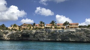 Un hôtel situé sur la côte, composé de plusieurs bâtiments, bordé de palmiers et adossé à une falaise rocheuse.
