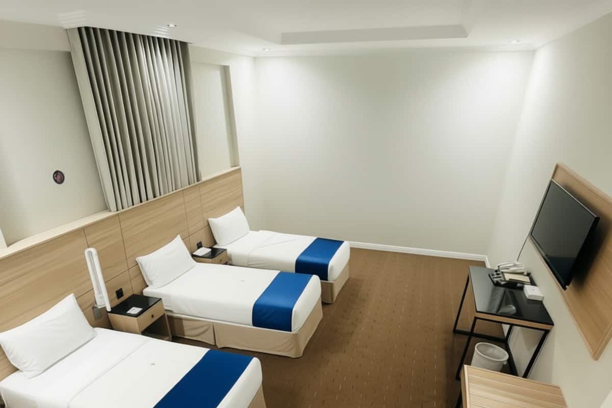 Ein Hotelzimmer mit zwei Betten, einem Fernseher, einem Schreibtisch und einem Fenster mit Jalousien.