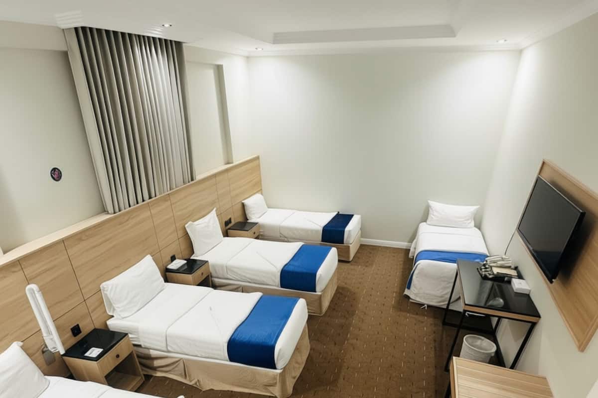 Ein Hotelzimmer mit vier Einzelbetten, einem Fernseher, einem Schreibtisch und einem Badezimmer.