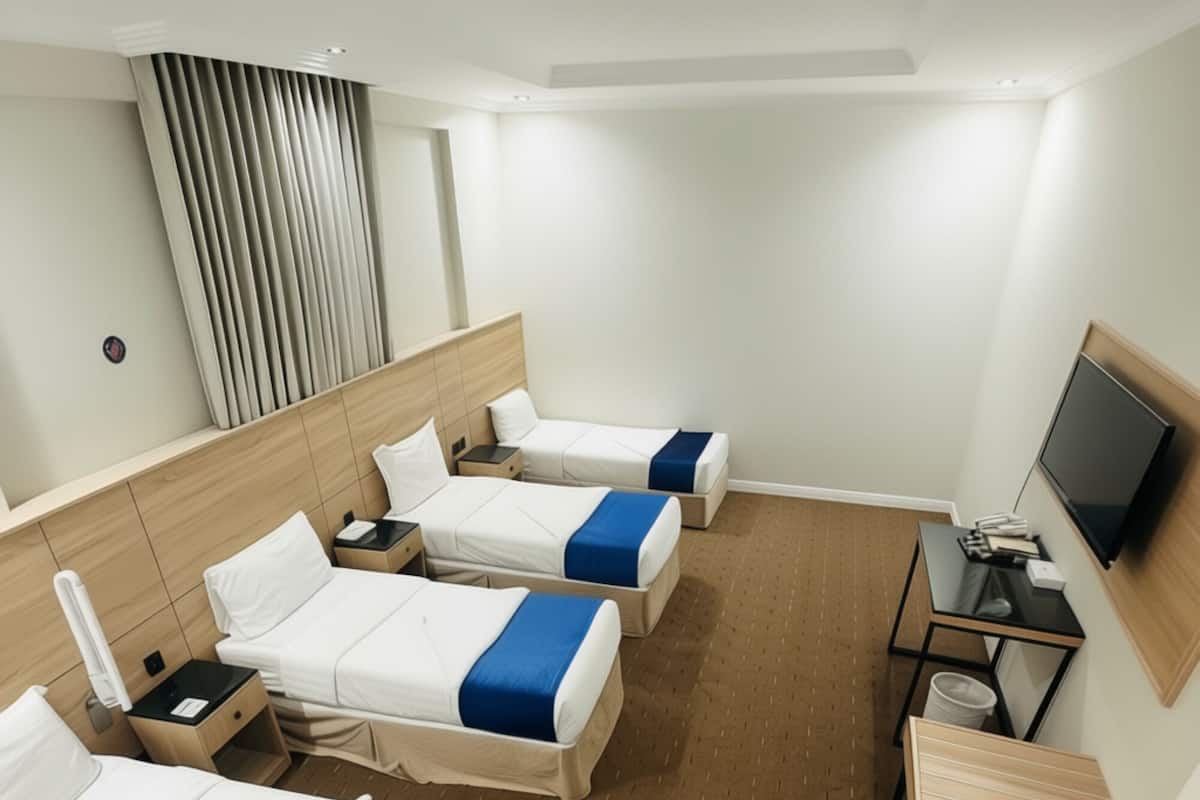 Ein Hotelzimmer mit drei Betten, einem Fernseher und einem Schreibtisch.