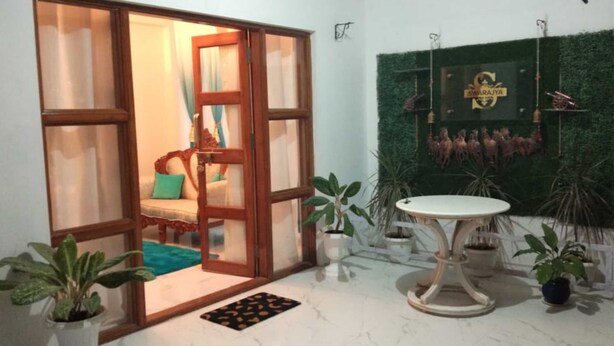 Una habitación con puerta de vidrio corredera que da a un rincón tranquilo con sofá y cojines. Hay una mesa redonda con tapa blanca y un adorno colgante en la pared.