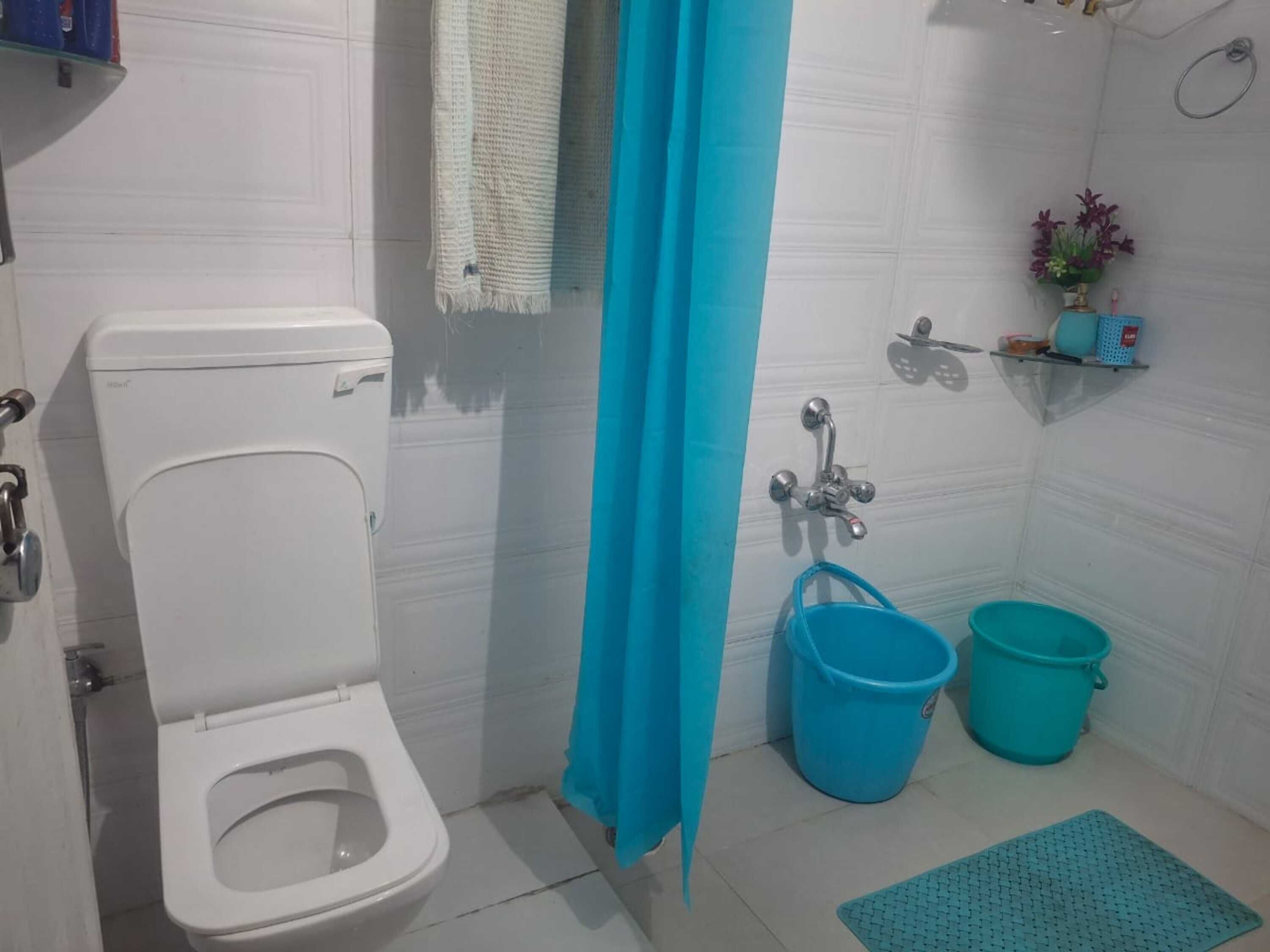 Une salle de bain comprenant des toilettes, un rideau de douche, un lavabo avec un robinet et deux seaux.
