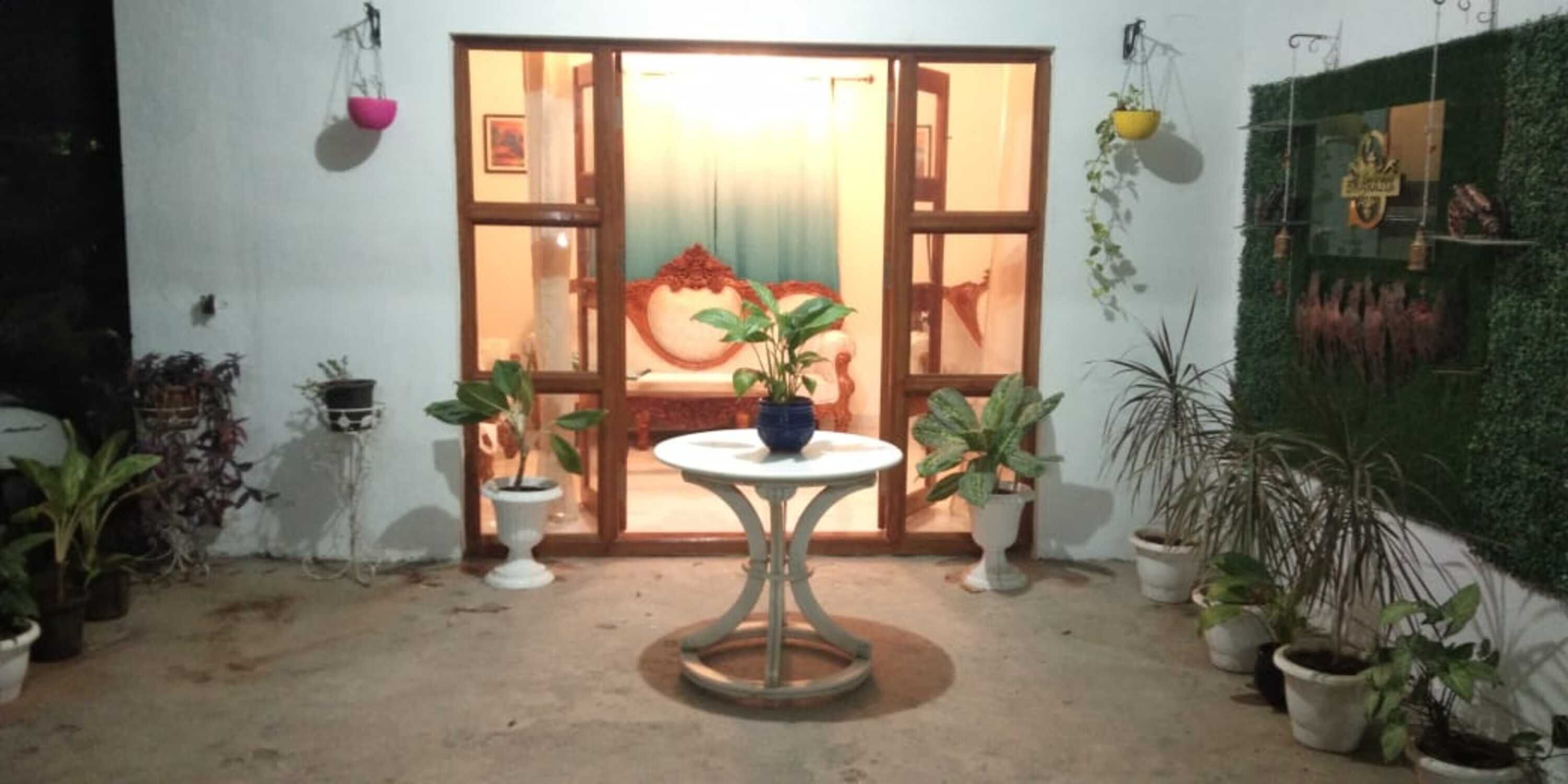 Een kamer met een ronde tafel, potplanten en een groot raam met gordijnen.