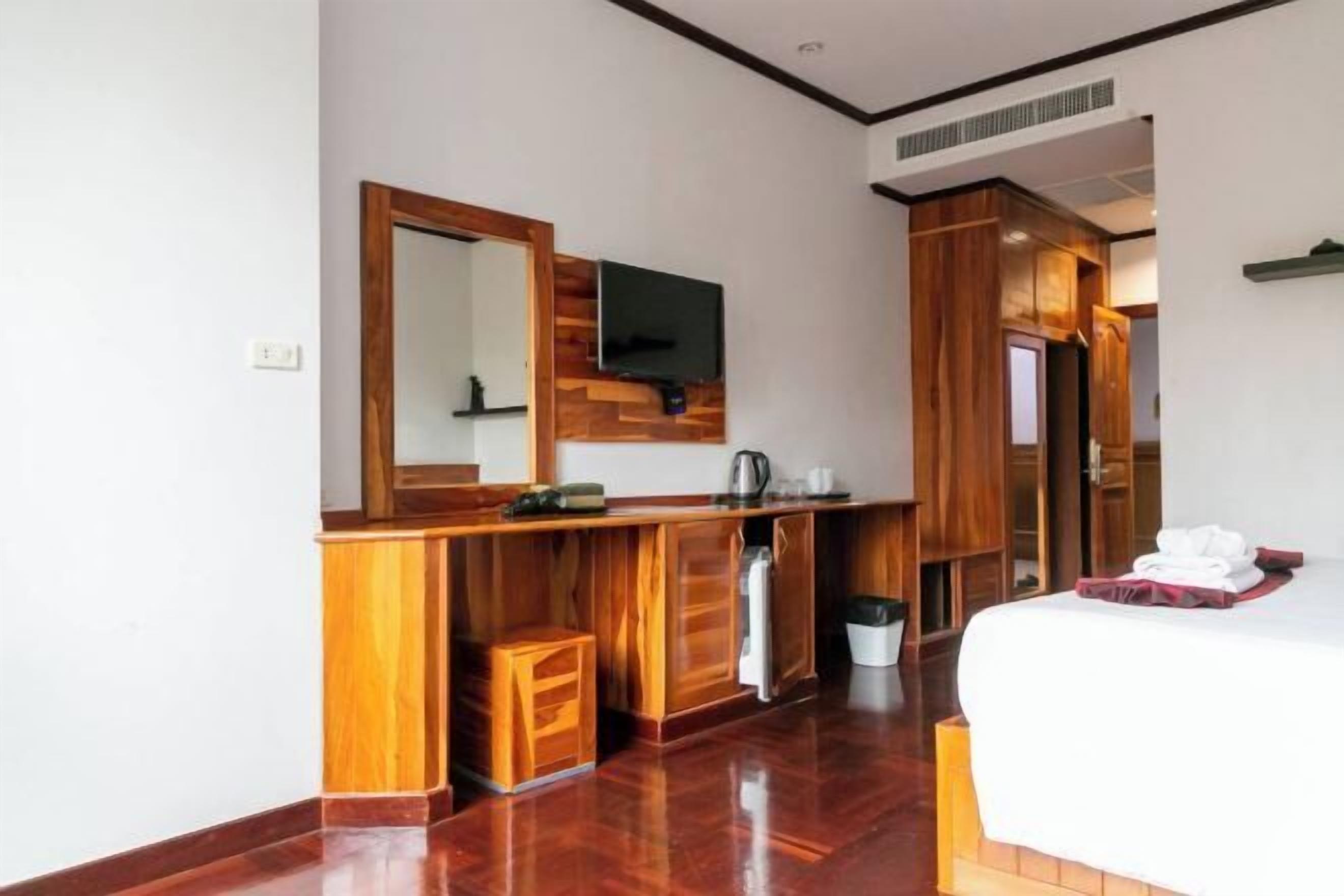Une chambre d’hôtel avec une coiffeuse en bois, un grand miroir, un téléviseur fixé au-dessus, un lit avec du linge de maison blanc et une armoire en bois.