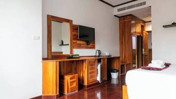 Une chambre d’hôtel avec une coiffeuse en bois, un grand miroir, un téléviseur fixé au-dessus, un lit avec du linge de maison blanc et une armoire en bois.
