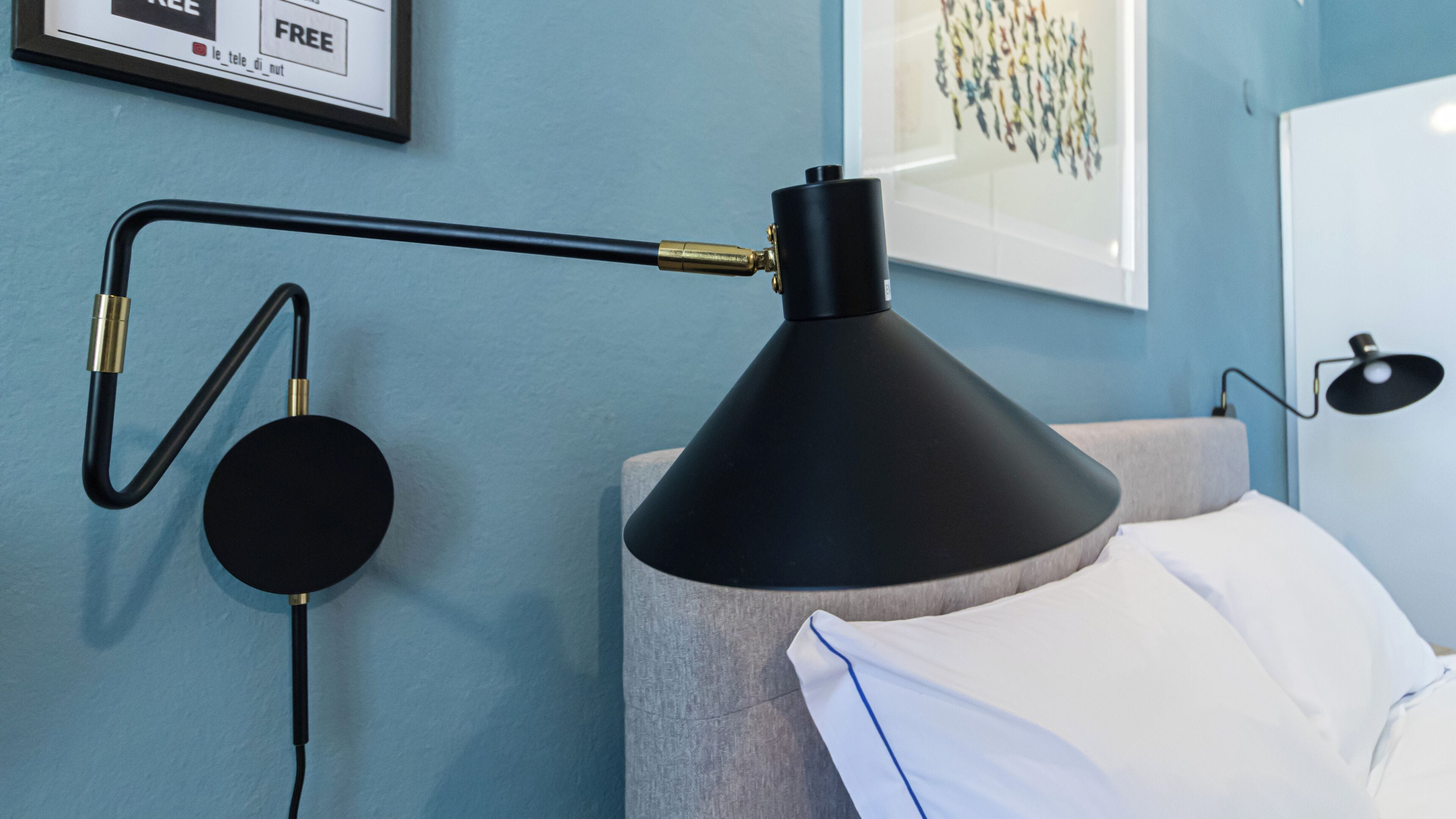 A modern room with a black desk lamp, a framed artwork, and a bed with a white pillow.