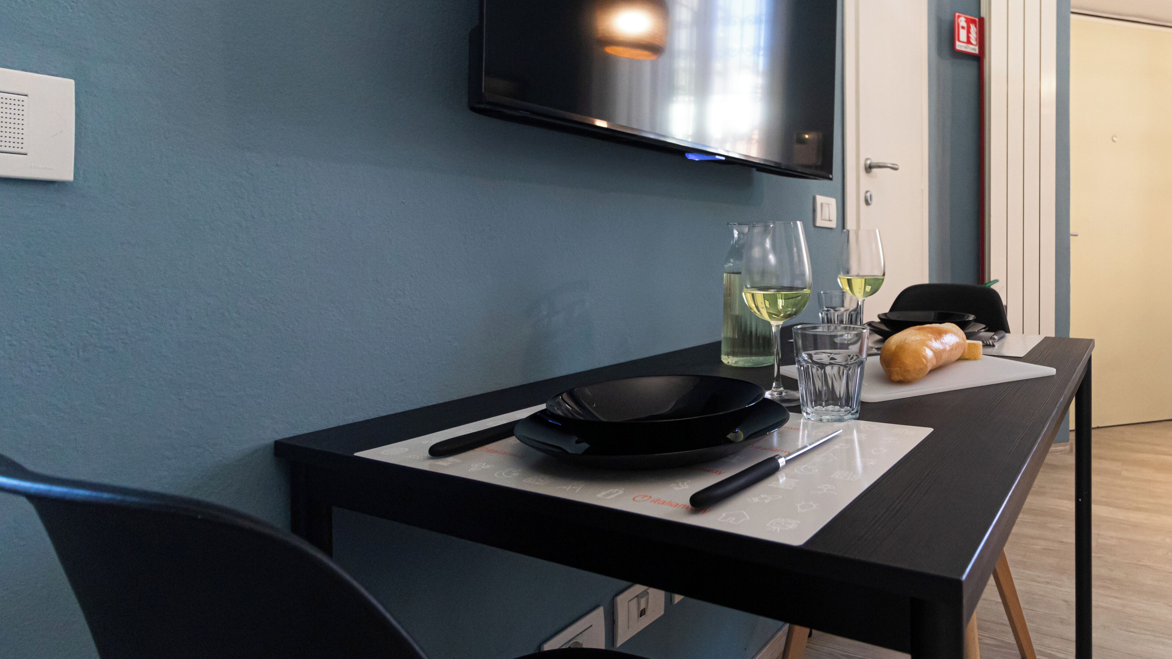 A dining table with a black pan, knife, and two wine glasses with a bottle of white wine.