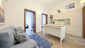 A compact living space with a kitchenette, a sofa with floral cushions, and a blue patterned rug. - Apartamenty Sun & Snow Pomorska Przystań (Kołobrzeg)
