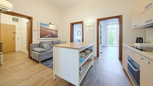 A modern kitchen with a built-in oven and a dining area with a grey sofa and a wooden table. - Apartamenty Sun & Snow Pomorska Przystań (Kołobrzeg)