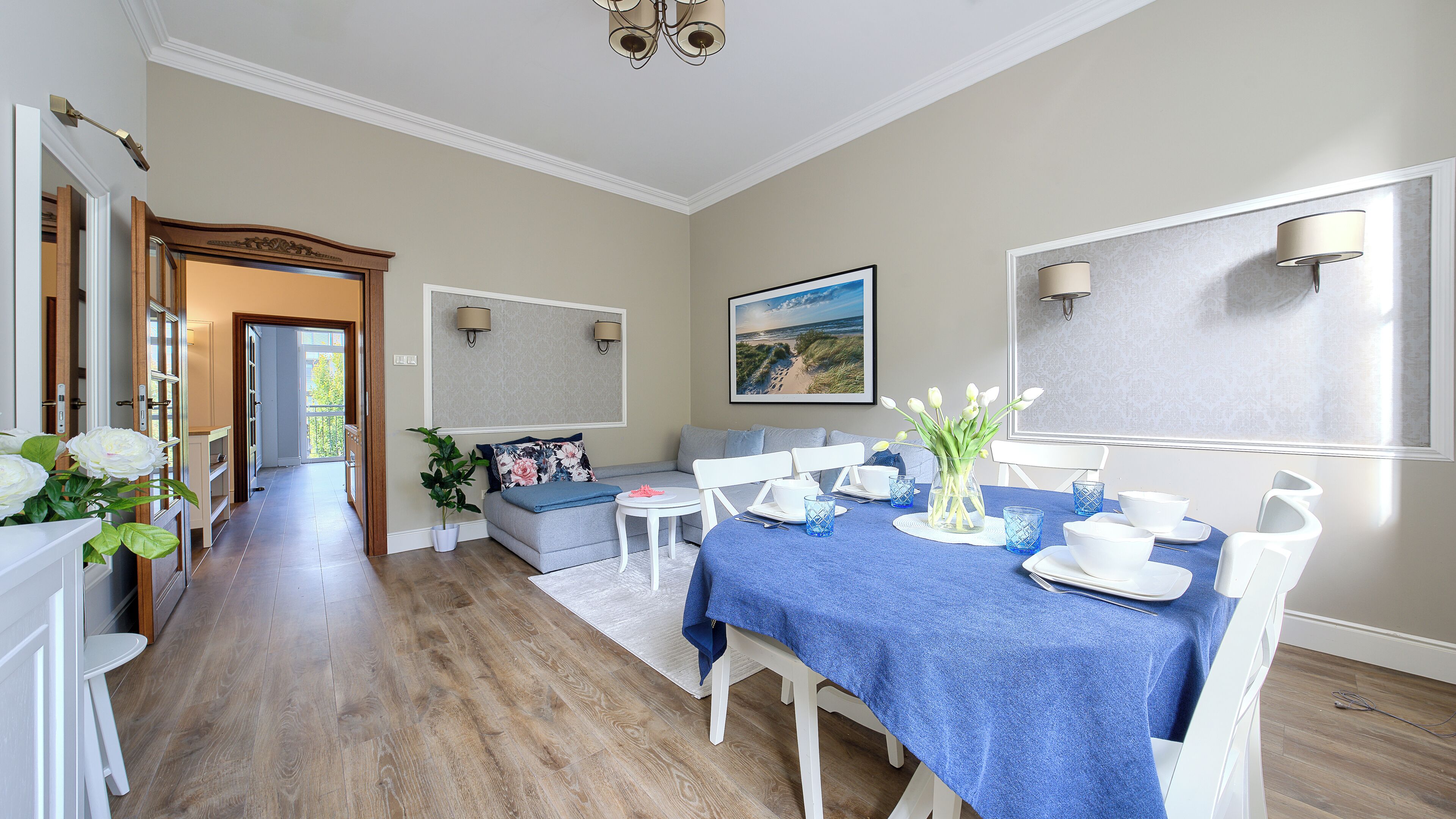 A dining area with a blue tablecloth, white chairs, and a vase of flowers.