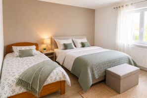 Un dormitorio con dos camas, una mesita de noche con lámpara, una ventana con cortinas y un radiador.