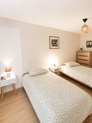 Ein Schlafzimmer mit zwei Einzelbetten, einem Nachttisch mit Lampe, einer Kommode und einem gerahmten Bild an der Wand.