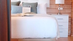 A bedroom with a large bed, a bedside table with a lamp, and a wooden wall. - Cabaña 5 Maceira en Bueu (Bueu)