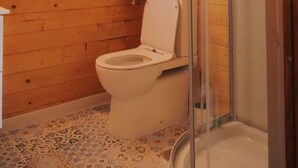 A compact wooden cabin bathroom with a toilet, a glass shower enclosure, and a window with a curtain. - Cabaña 5 Maceira en Bueu (Bueu)