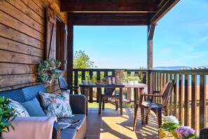 A wooden deck with a table and chairs, a sofa with cushions, and a view of the landscape.