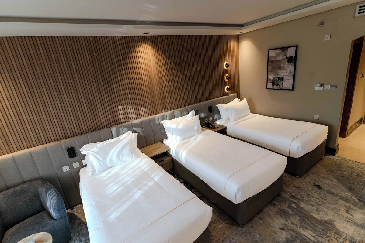 A hotel room with three single beds, a grey sofa, and a wooden panel wall.