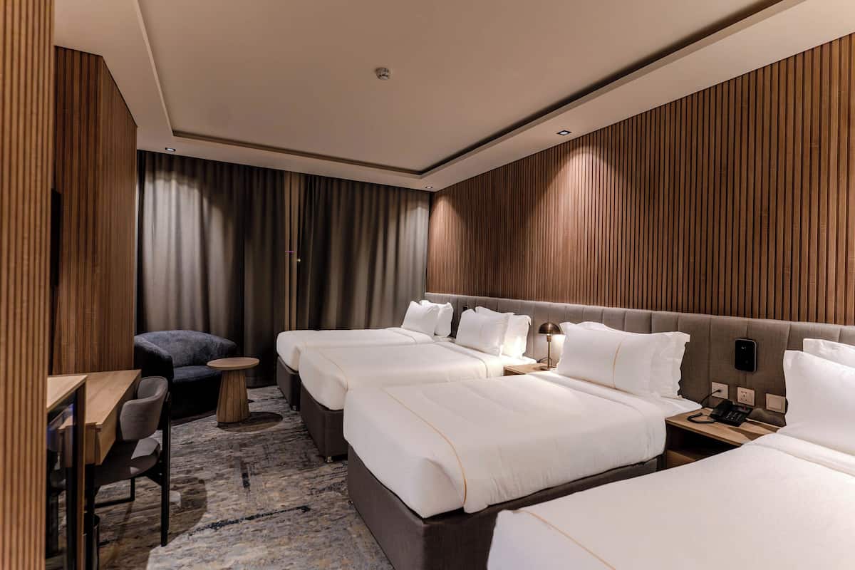 A hotel room with two beds, a desk, a chair, and a small table.