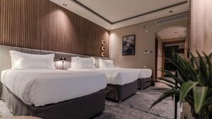 A hotel room with two beds, a wooden panel wall, a marble floor, and a plant. - Hill Hotel (Madinah)